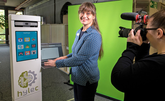 Rapidmooc mit Benutzerin vor einem angeschlossenen Laptop, Greenscreen im Hintergrund