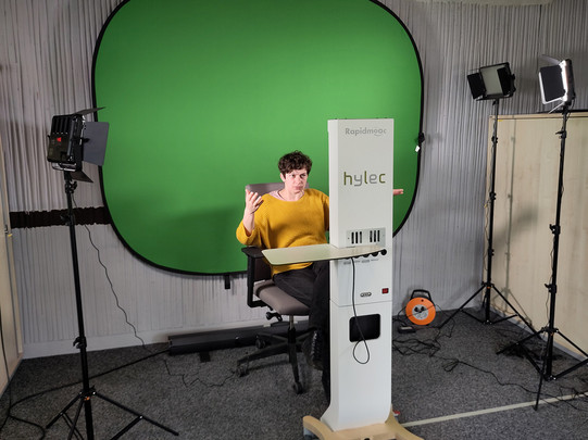 Hintergrund Greenscreen, vorne Rapidmooc, dazwischen sitzt eine Frau und benutzt die Videostation