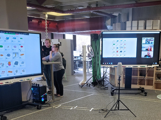 Zwei Smartboards im Raum E1. Der Inhalt eines Workshops wird angezeigt und zusätzlich läuft auf dem rechten Smartboard ein Zoomcall für die Online-Teilnehmer