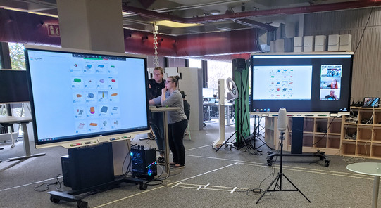 Zwei Smartboards im Raum E1. Der Inhalt eines Workshops wird angezeigt und zusätzlich läuft auf dem rechten Smartboard ein Zoomcall für die Online-Teilnehmer