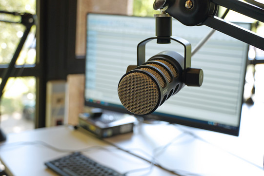 Podcaststation, ein Mikrofon im Vordergrund, der PC-Arbeitsplatz im Hintergrund.