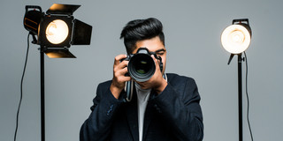 Junger Mann hält Kamera auf Betrachter, links und rechts Scheinwerfer